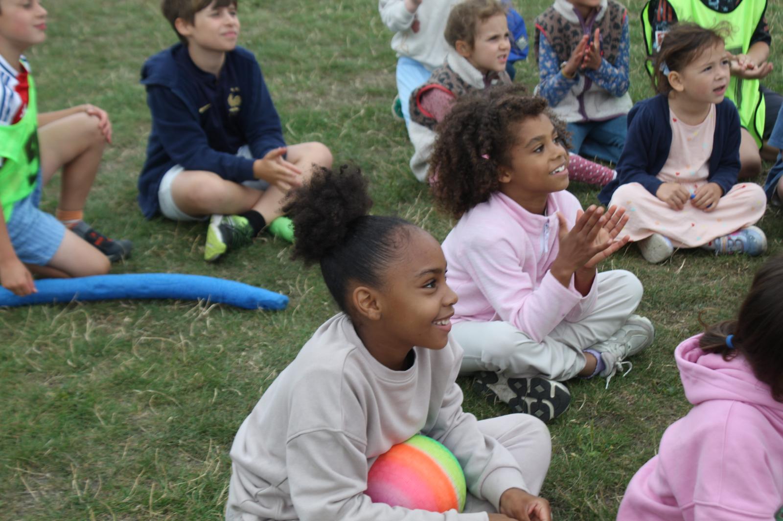 Photo of happy, smiling children sitting on the grass and listening attentively to a coach