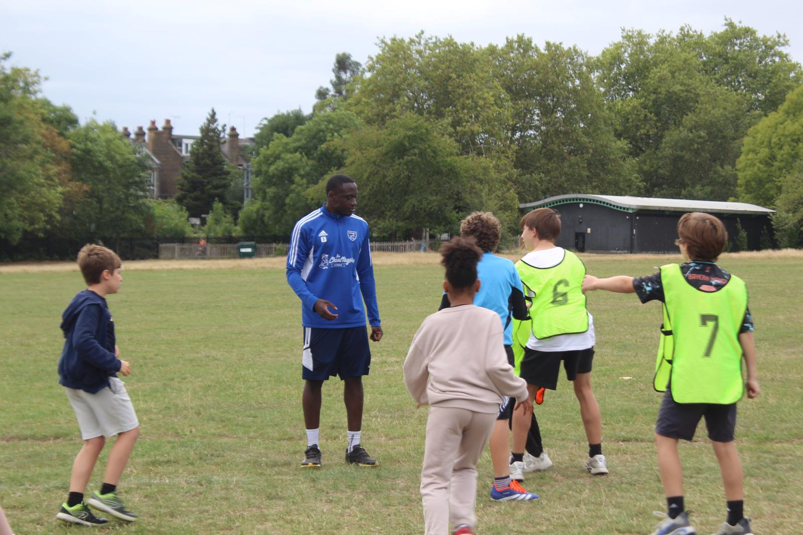 Photo of a group of children, two of whom are wearing yellow bibs, playing around a coach in a public park